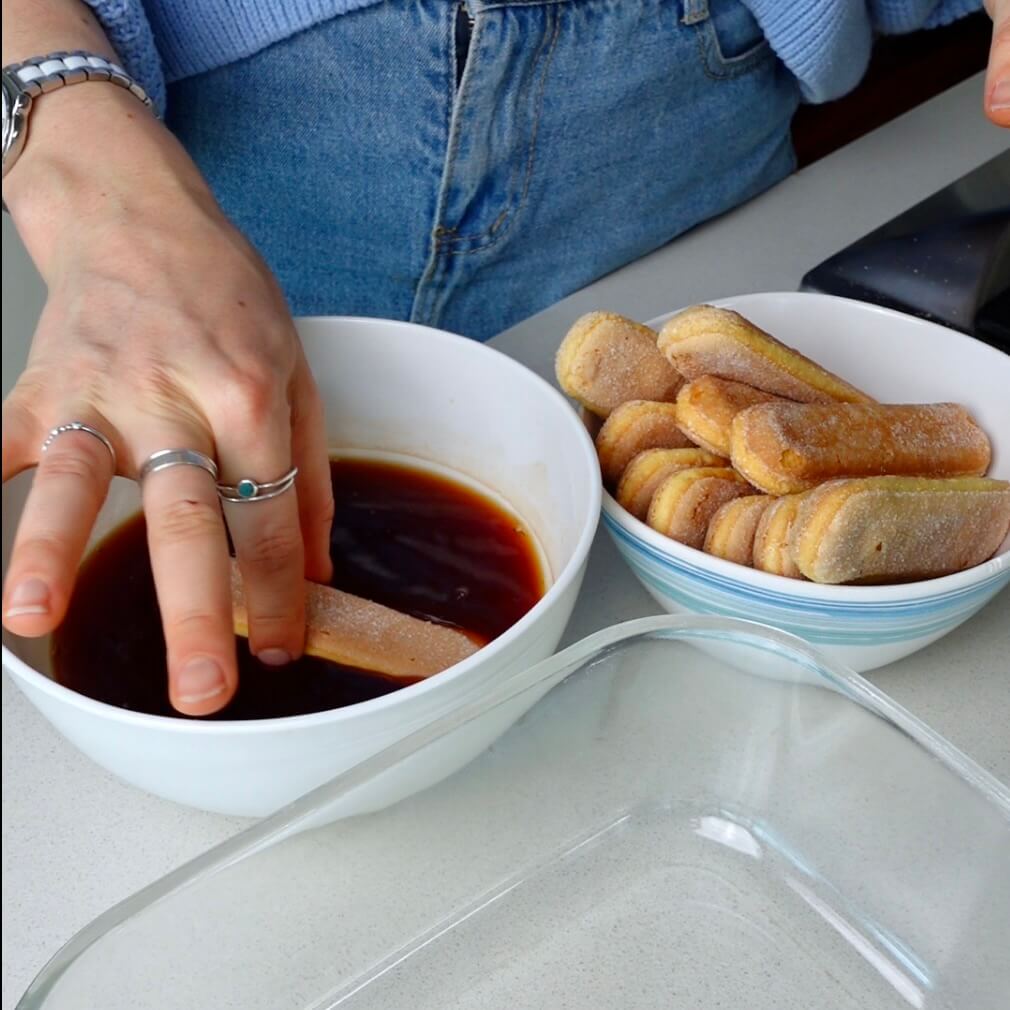 dipping lady finger biscuits into a bowl of tea to make a chai tea tiramisu